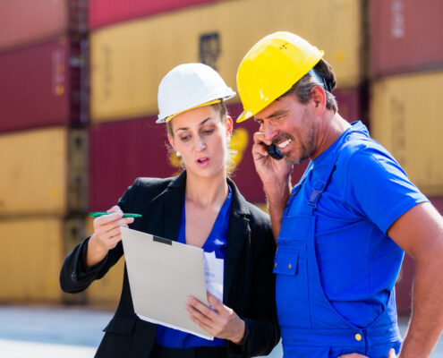 Male and Female Employees in logistics company shipping containers with clipboard talking on spectralink phone